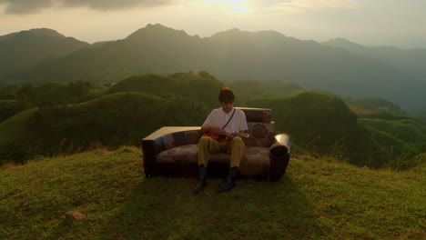 man playing ukulele on mountaintop at sunset
