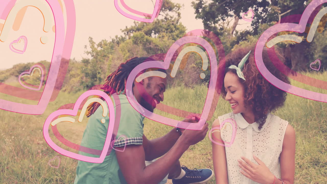 Man proposing to woman with pink heart animation over outdoor scene