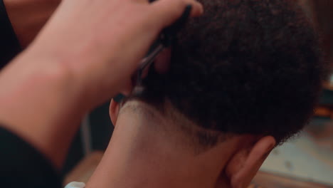 amazing slow motion shot of a close-up of a haircut by a professional barber in a barbershop doing a line design with a razor to a young afro man during the afternoon