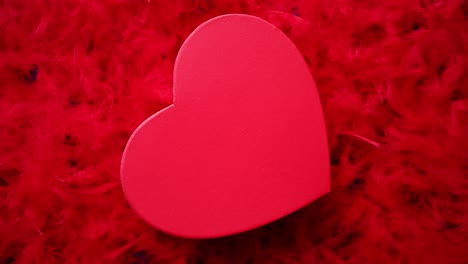 heart shaped boxed gift  placed on red feathers background