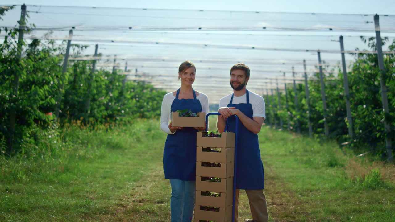 hermosa pareja buscando cámara en la temporada de verano con caja de fruta fresca en la granja.
