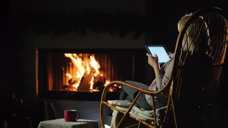 young woman resting by the fireplace using a tablet