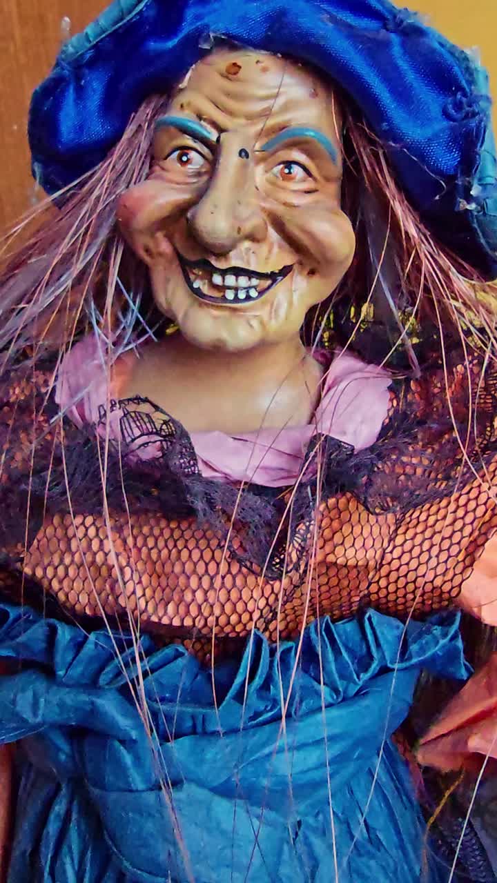 Vertical macro shot of a witch doll with a blue hat, missing teeth, and colorful lace clothing, showing a creepy grin