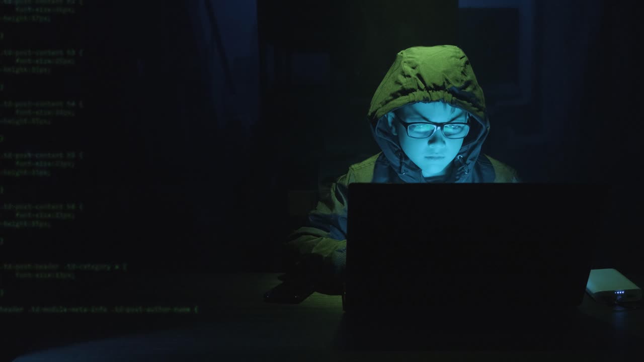 Computer Code Superimposed Over Male Kid Hacker At Work On A Laptop Software At Night. medium shot, zoom-in