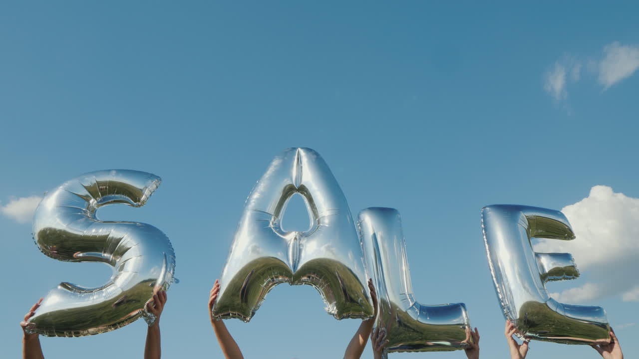 여러 사람이 문자 형태로 풍선을 들고 판매 4k 비디오라는 단어를 구성합니다.