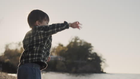 A-purposeful-boy-of-two-years-throws-a-stone-into-the-sea.-Side-view,-slow-motion-video