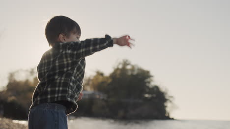 a purposeful boy of two years throws a stone into the sea. side view, slow motion video