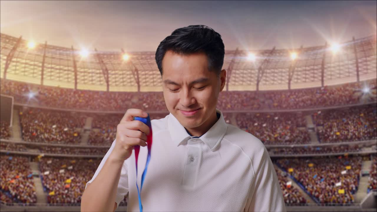 금메달을 입고 카메라를 향해 미소 짓는 아시아 남자가 스타디움에서 첫 우승자로 자랑스럽게 승리합니다.