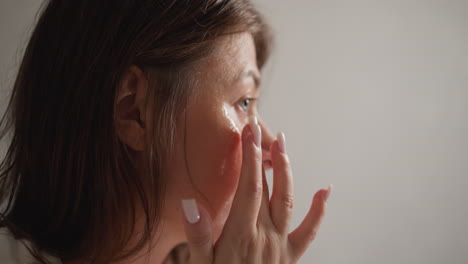 brunette female smears face mask with fingertips in shower closeup. woman with dark hair massages face with transparent nourishing cream slow motion