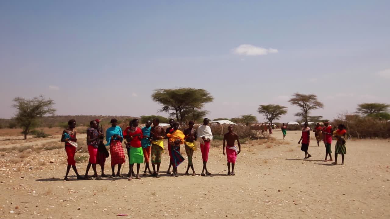 Amazing shot of Maasai local tribe in traditional colorful clothing dancing, jumping, clapping and singing in small village in the drylands of African Savanna, Kenya, Africa.