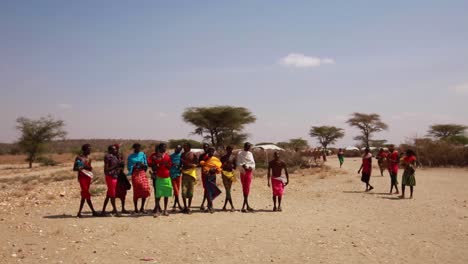 amazing shot of maasai local tribe in traditional colorful clothing dancing, jumping, clapping and singing in small village in the drylands of african savanna, kenya, africa.