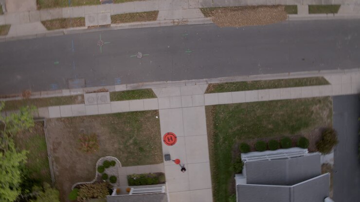 Veduta aerea di un pilota di drone che fa volare il drone da un vialetto residenziale mentre il drone gira sopra la strada.