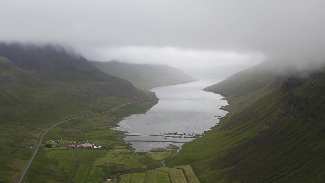 Luchtopname van de nadering van de schilderachtige Sugandafjordur Fjord op IJsland, tussen groene heuvels tijdens een mistige dag.