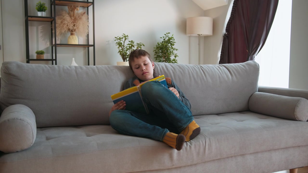 Un bambino assorto nella lettura di un libro mentre è seduto comodamente su un divano, godendosi il tempo libero.