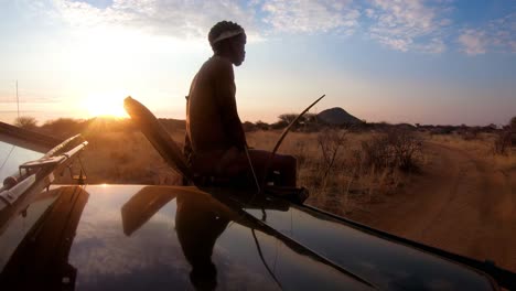 a native spotter guide sits on the front of a safari jeep vehicle spotting wildlife on the plains of africa at sunset 1