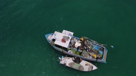 drone rastreando dos barcos de pesca llenos de actividad preparándose para lanzar redes en la bahía de cerca, de arriba hacia abajo