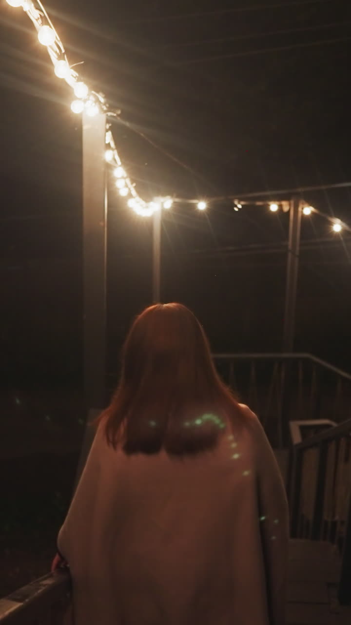 una mujer camina por una larga escalera de madera. una mujer joven con una manta va a pasear por el campamento en la noche de otoño. las luces decorativas se encienden de manera iluminadora