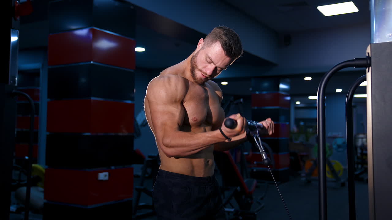 Handsome strong young bodybuilder works out on sport equipment. Strong abs. Modern gym background. Video from the side.