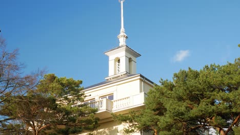 White-building-tower-top-with-green-conifer-tree-in-Palanga,-Lithuania