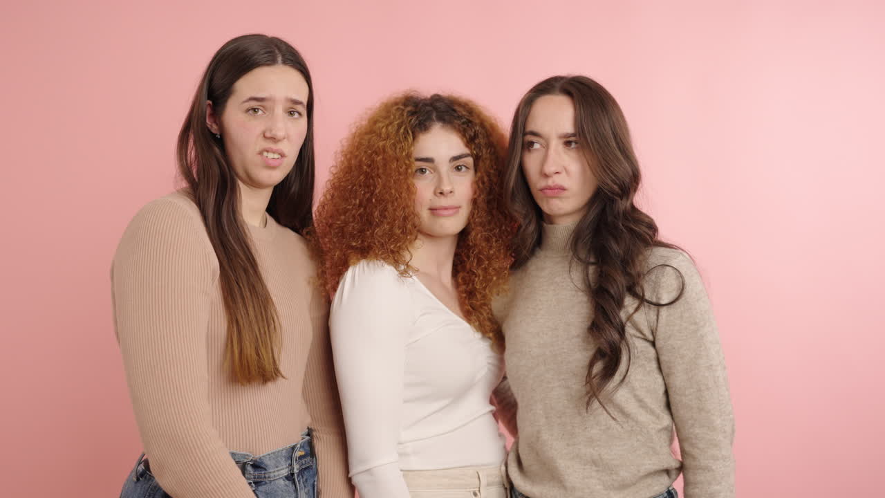 Three young women showing disgust expressions on pink background
