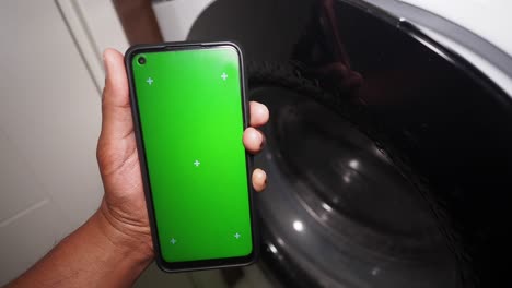 person holding a green screen phone near a washing machine