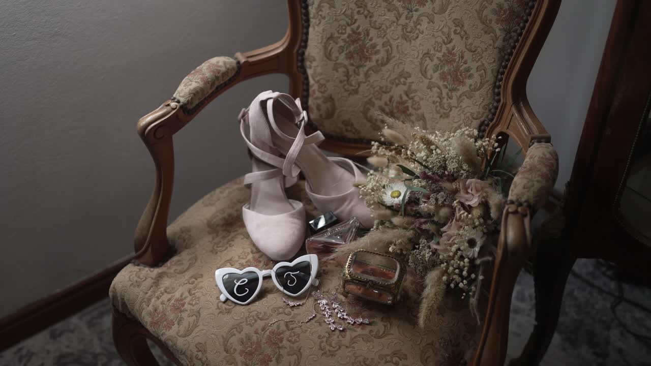 Wedding shoes bouquet and accessories laid on ornate vintage chair indoors