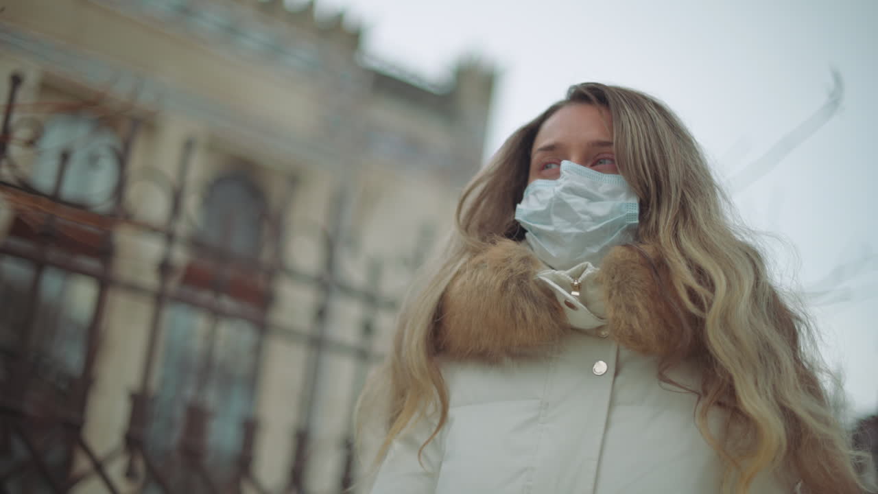 A woman in a white winter coat carefully gets off a medical mask outdoors on a cold day
