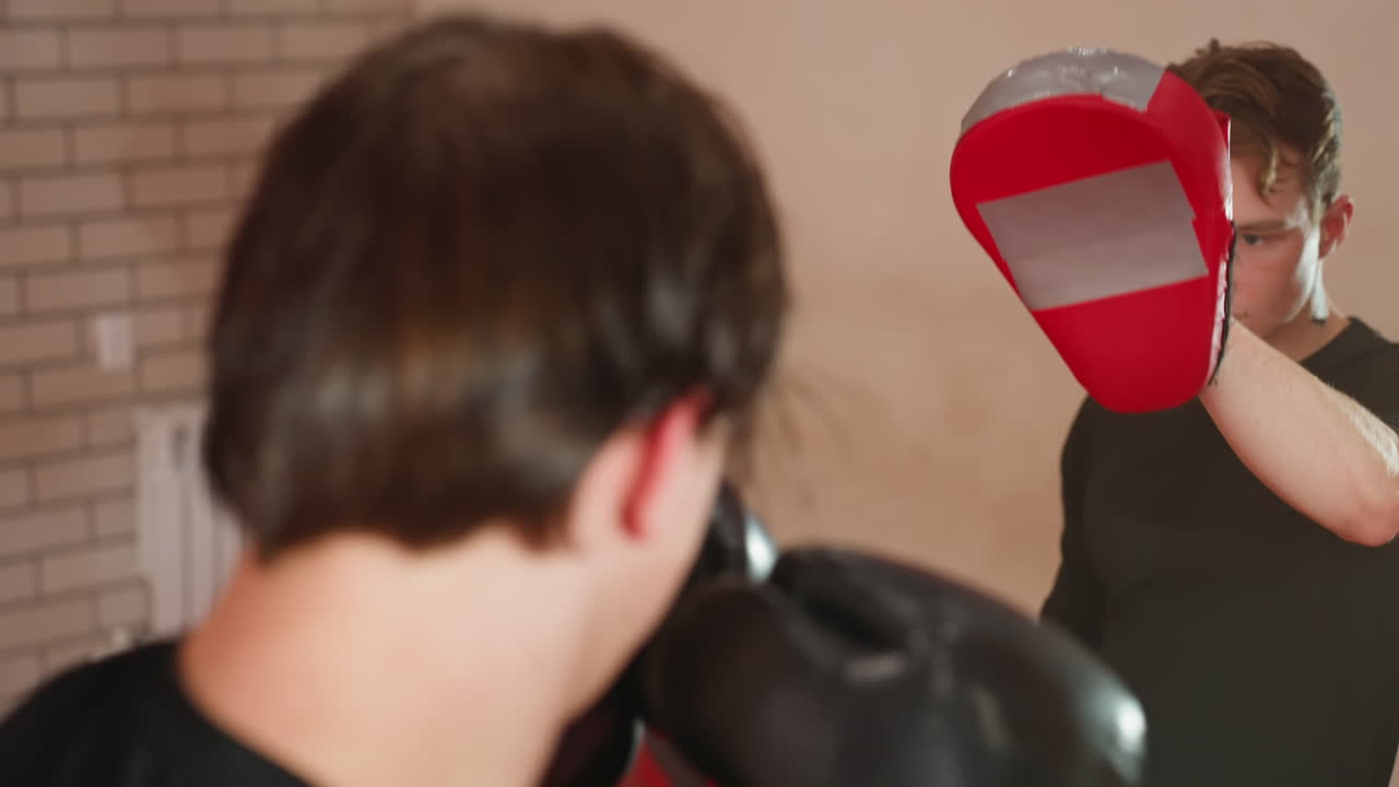 MMA fighter trains with coach holding red punching mitt during sparring session inside gym, practicing strikes with focus, strength, precision, and discipline to improve technique, combat performance