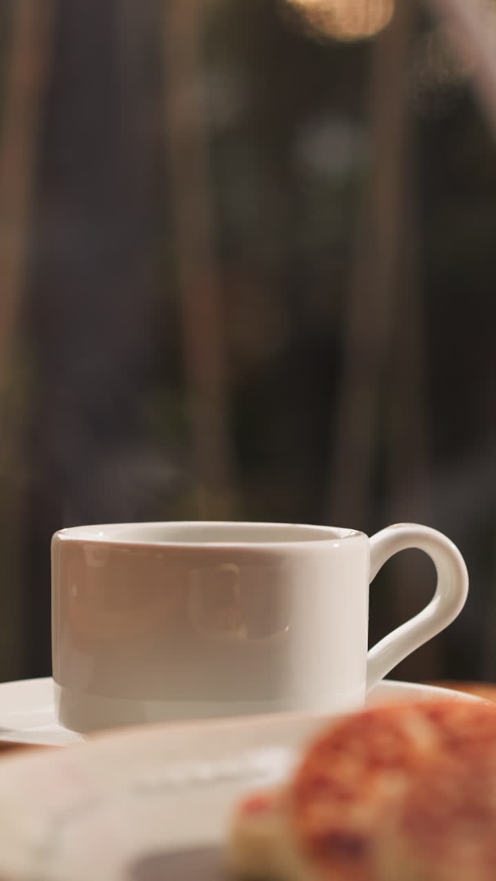 Tea cup on table against panoramic window. Surrounding array of breakfast dishes creates inviting scene beckoning with revitalizing drinks and delicious food