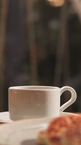 tea cup on table against panoramic window. surrounding array of breakfast dishes creates inviting scene beckoning with revitalizing drinks and delicious food