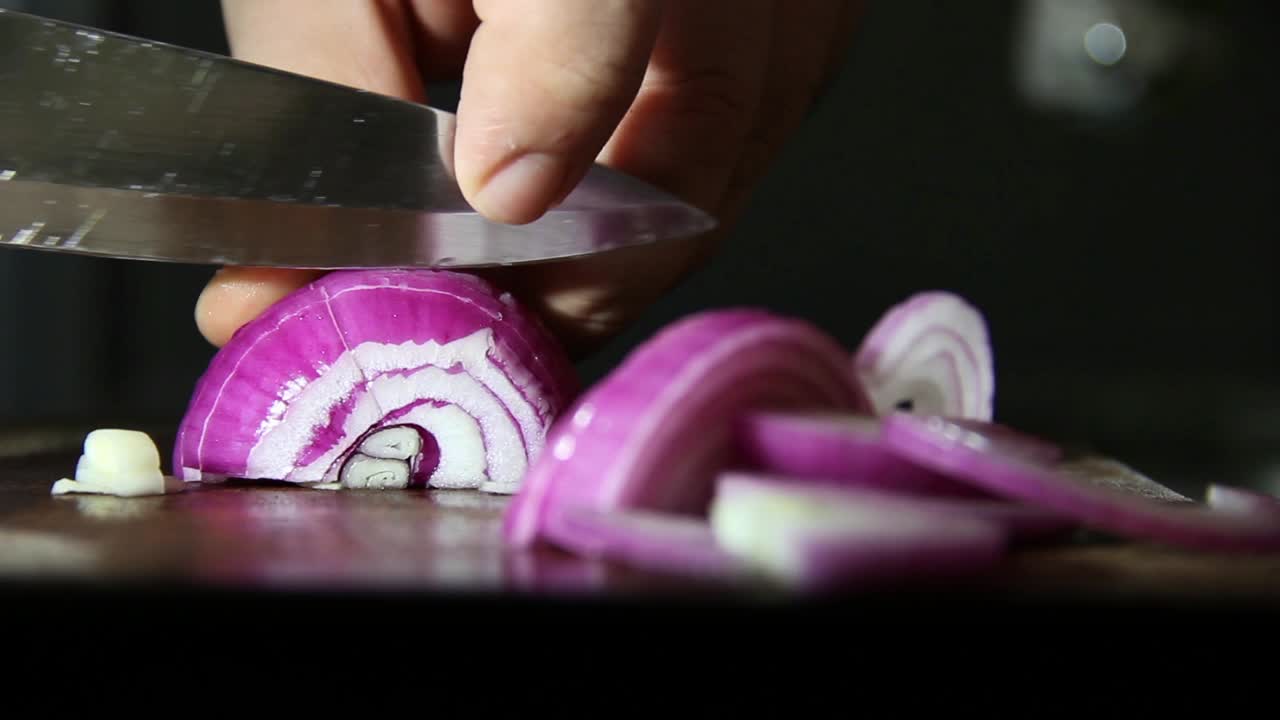 Primo piano di mani che tagliano una cipolla rossa su un tagliere