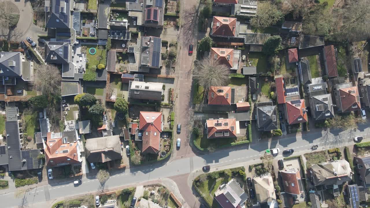 Top down aerial of a wealthy neighborhood with photovoltaic solar panels on the rooftops of homes. A green park is adjacent to the beautiful block