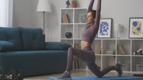 Una-Mujer-Atlética-Está-Haciendo-Una-Pose-De-Guerrero-En-Un-Entrenamiento-De-Yoga-En-Casa-Estirando-Las-Manos-Hacia-Arriba-Una-Deportista-Delgada-Con-Un-Estilo-De-Vida-Deportivo-Y-Saludable-En-La-Habitación