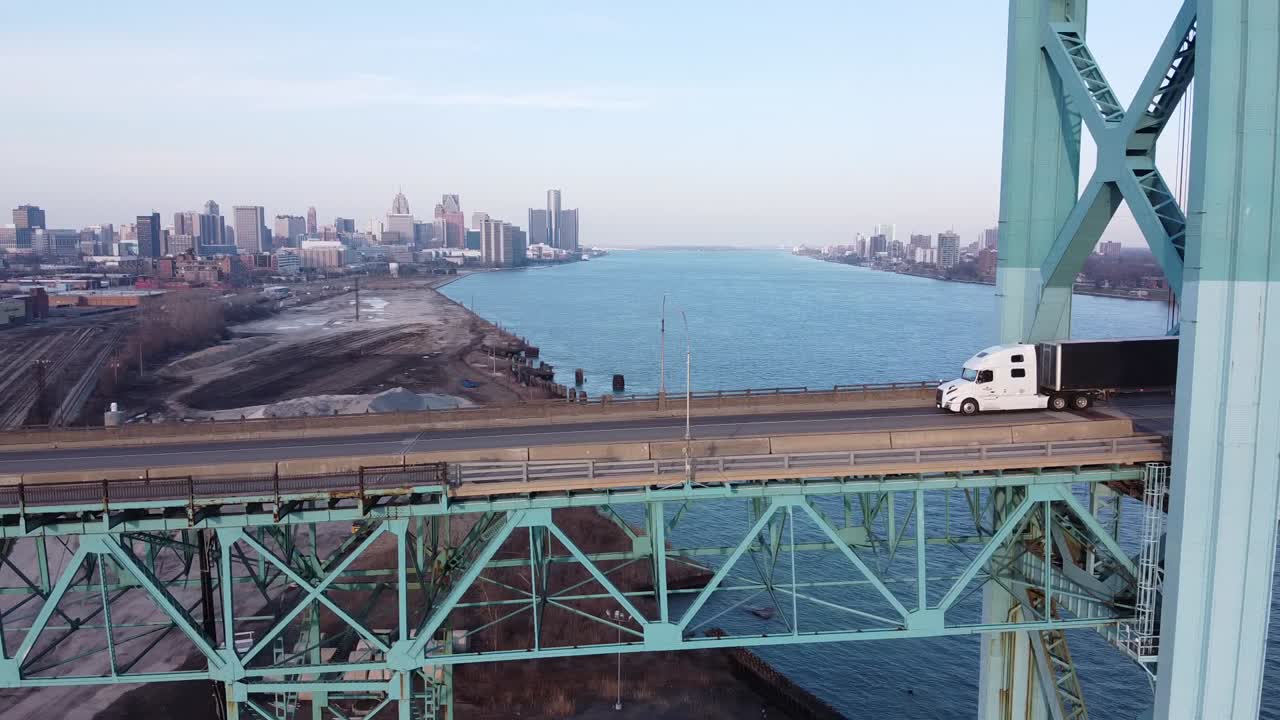A Modern Big Rig Semi Truck Driving Along The Ambassador Bridge To Canada With Detroit Skyline In The Background.-aerial shot