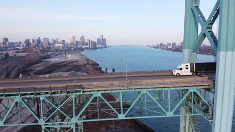 a modern big rig semi truck driving along the ambassador bridge to canada with detroit skyline in the background.-aerial shot