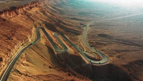 several cars descend on the black asphalt with hairpin bends on the highway 40 in mitzpe ramon in israel in the beautiful brown hill landscape