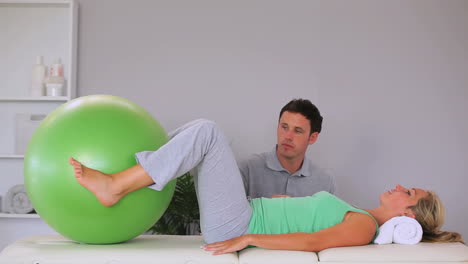 physiotherapist watching his patient move an exercise ball in between her knees