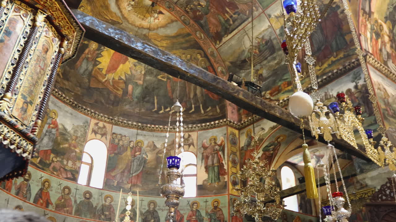 Explore the detailed frescoes and ornate chandeliers inside Bachkovo Monastery. The warm lighting highlights the intricate artwork, creating a serene, historical ambiance