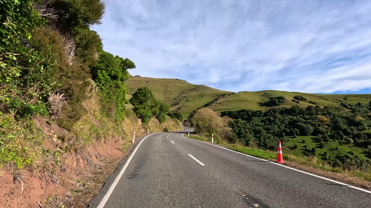 A serene drive along a rural highway in Akaroa, showcasing lush greenery and rolling hills under clear skies