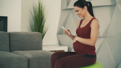 Schwangerschaft-Und-Mutterschaft.-Junge-Hübsche-Schwangere-Frau-In-Sportkleidung,-Die-Zu-Hause-Ihr-Telefon-Benutzt.