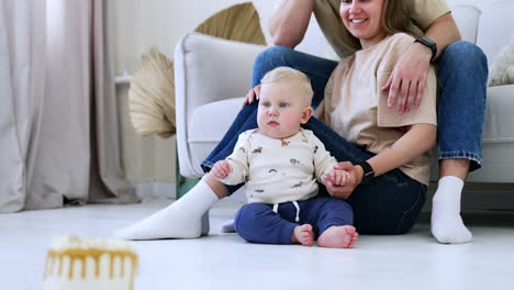 cute chubby baby boy sits on the floor near his parents. calm little kid sitting still looking around.