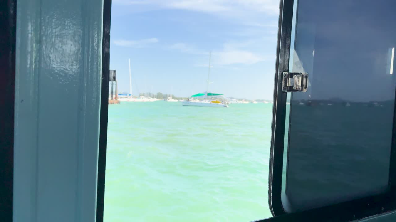 A tranquil scene of turquoise waters viewed through a boat window, capturing the essence of a sunny day in Phuket