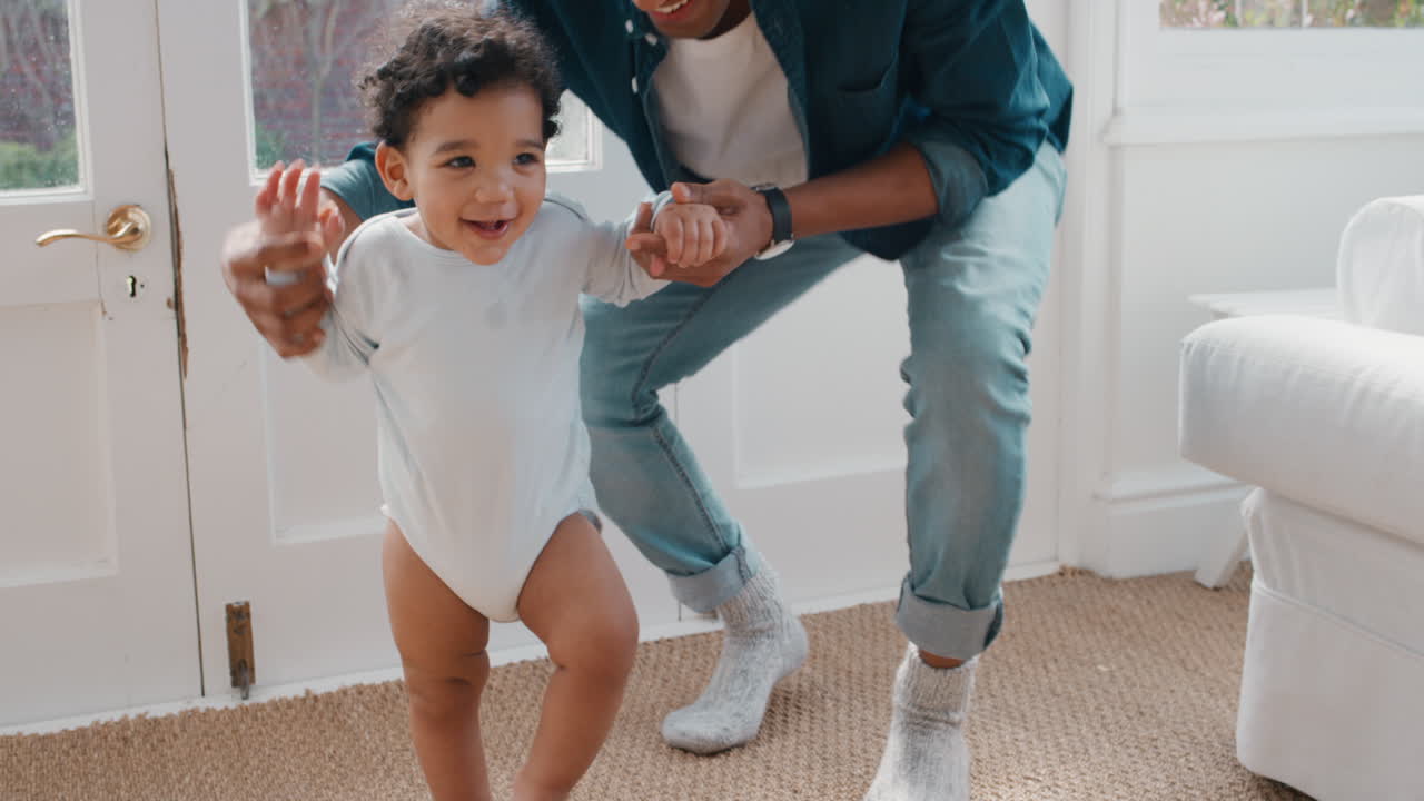 bebé feliz aprendiendo a caminar niño pequeño dando sus primeros pasos con el padre ayudando al bebé enseñando al niño en casa 4k
