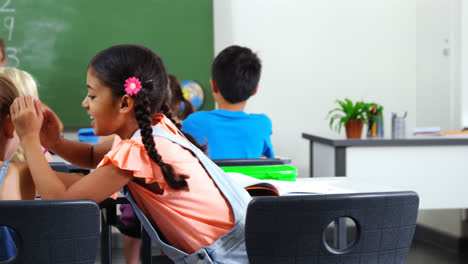 Schoolgirl-whispering-into-her-friend-s-ear-in-classroom