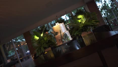 elegante pastel de boda adornado con flores y vegetación en una sala de recepción débilmente iluminada