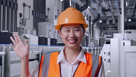 close up of asian female engineer with safety helmet smiling to camera and waving hand saying bye with water production in bottling factory