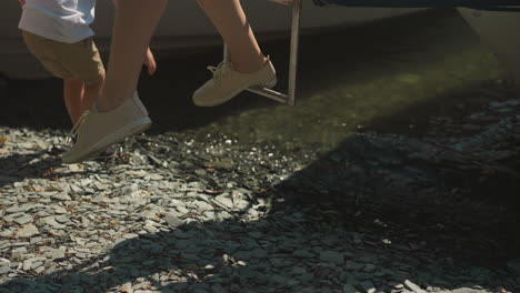 woman goes down steel ship ladder and little son plays with water on pebble beach in city port closeup. mother with little boy finish sea travel slow motion