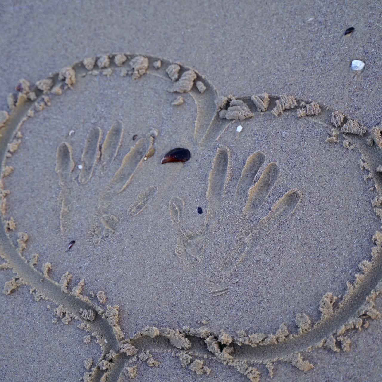 Woman is painting on wet sand. Top view of a heart written on a sandy beach. Young female drawing near the sea.