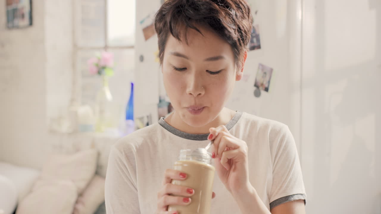 Asian girl indulging eating peanut butter from jar using spoon