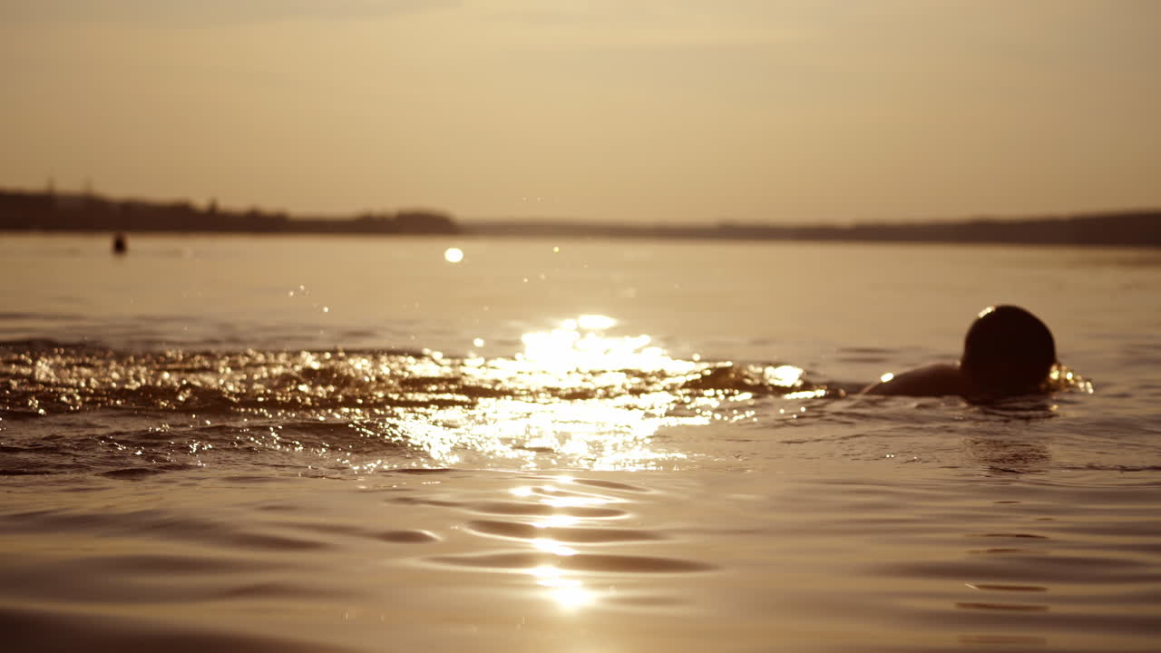 Boys are diving in the evening river at sunset. Silhouette of two kids swim under water in the evening during summer holidays.